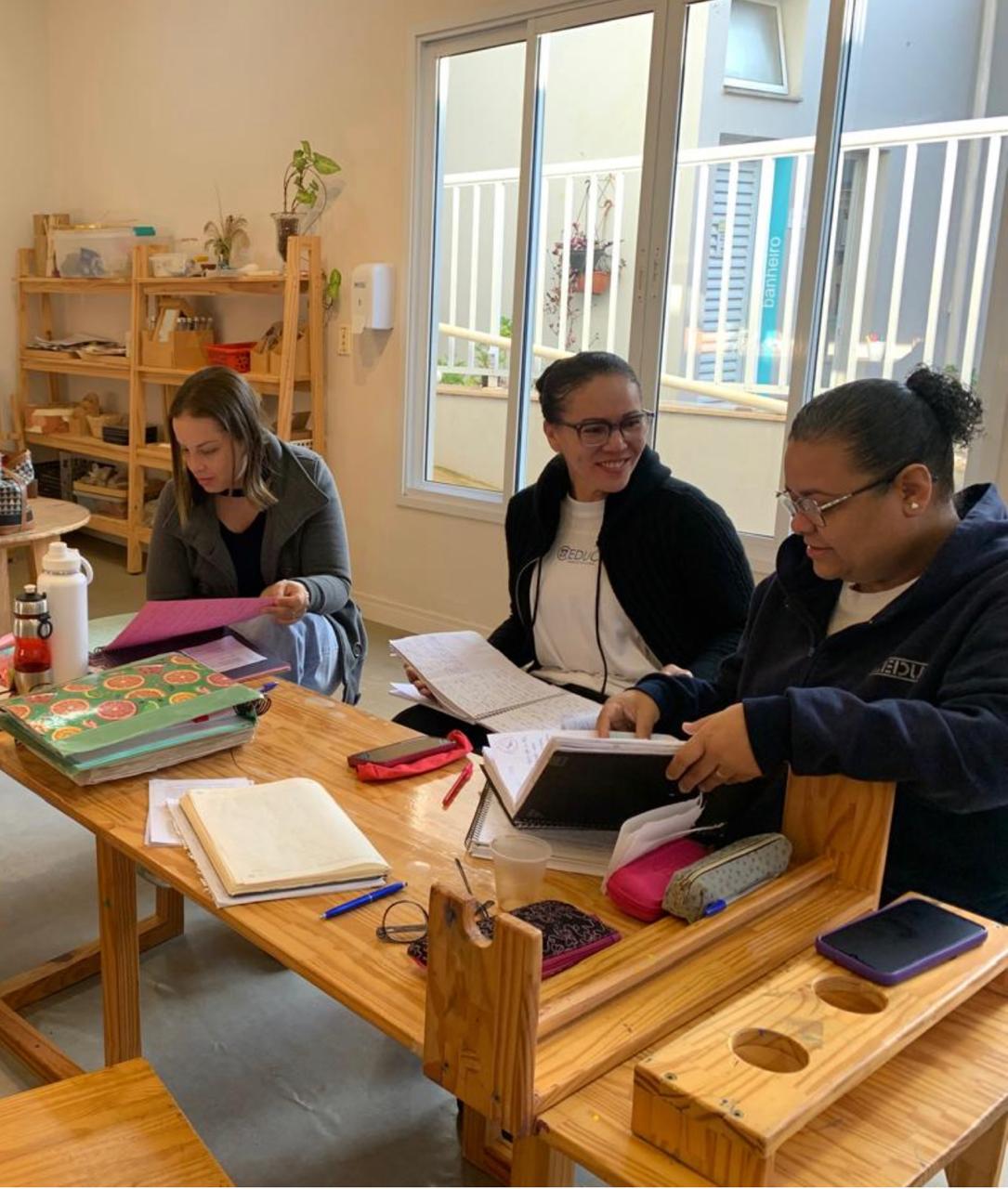 Educadoras em formação analisando registros pedagógicos em mesa